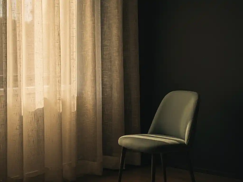 Ivoren linnen gordijnen filteren zacht natuurlijk licht tegen een houtskoolkleurige muur, met een salie groene accent stoel op de achtergrond.
