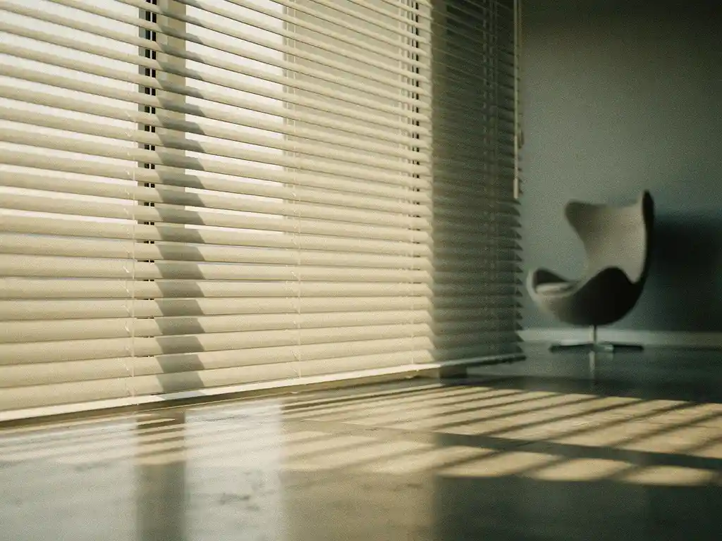 Horizontale jaloezieen filteren gouden middaglicht in een minimalistische showroom, met scherpe geometrische schaduwpatronen op gepolijst beton.